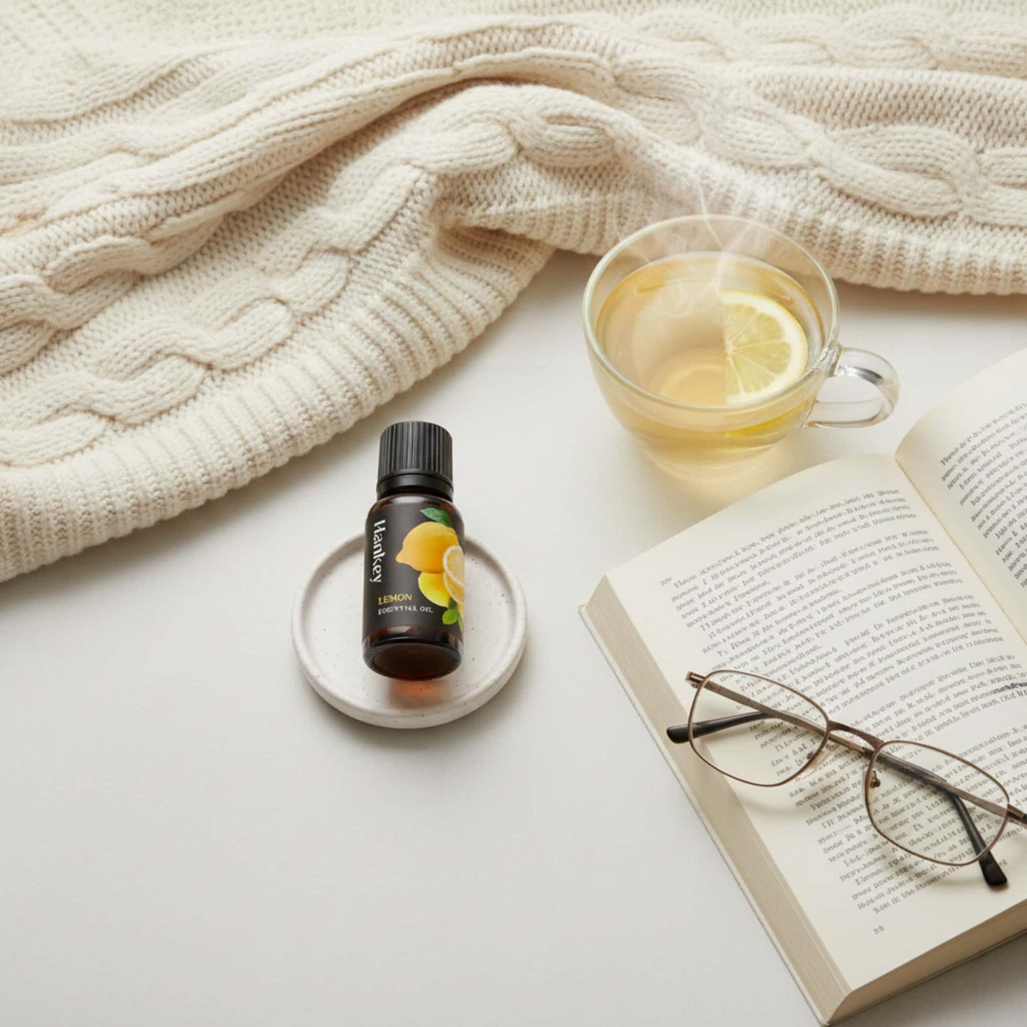 Lemon essential oil bottle next to an open book and a cup of tea, enhancing a cozy reading and relaxation moment.