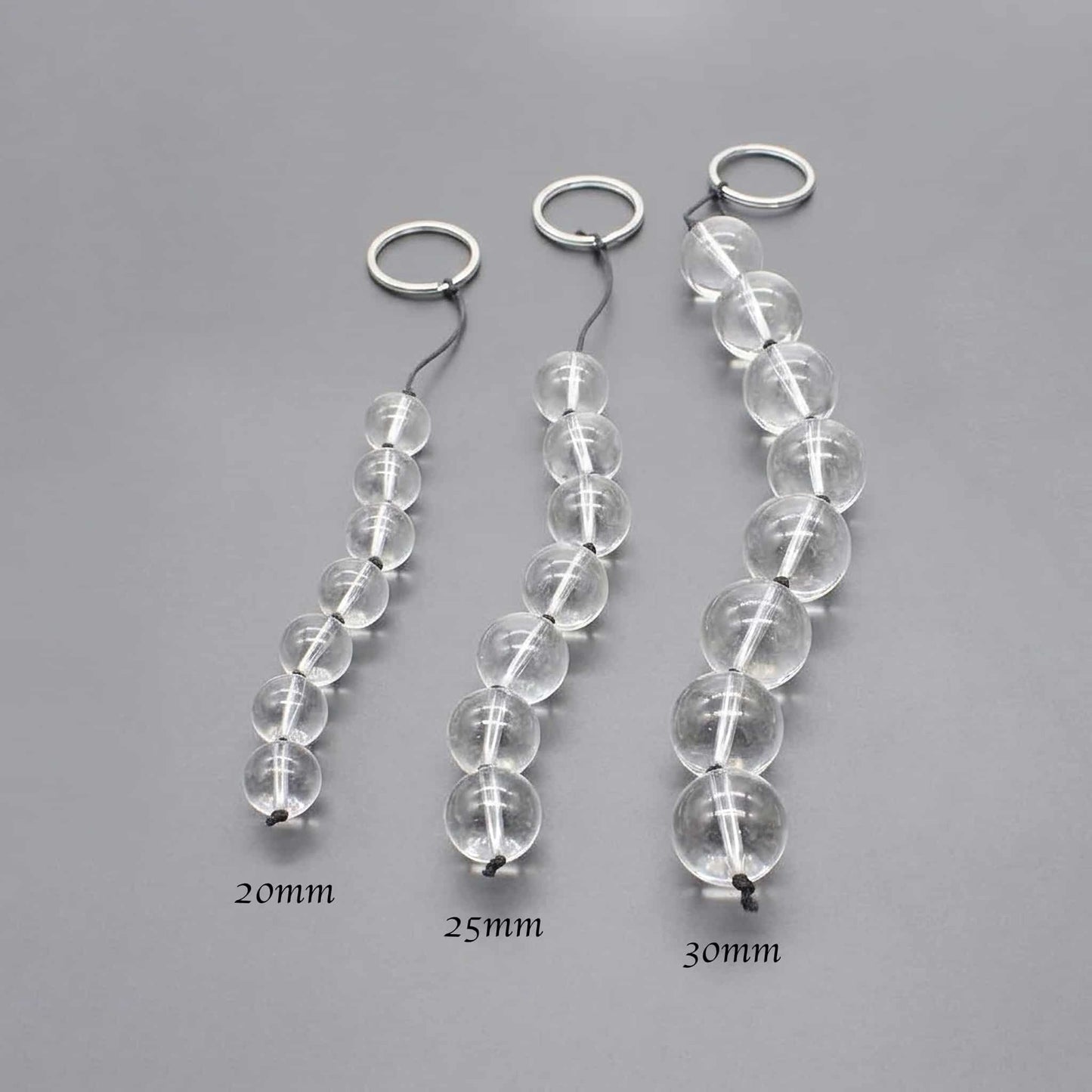 Demonstrate the gradation of pulled glass beads from the smallest to the largest size. Lining up four beads (e.g., 20mm, 25mm, 30mm) and shooting them at an angle highlights the difference in size. The background is a clean gray to make the beads stand out.