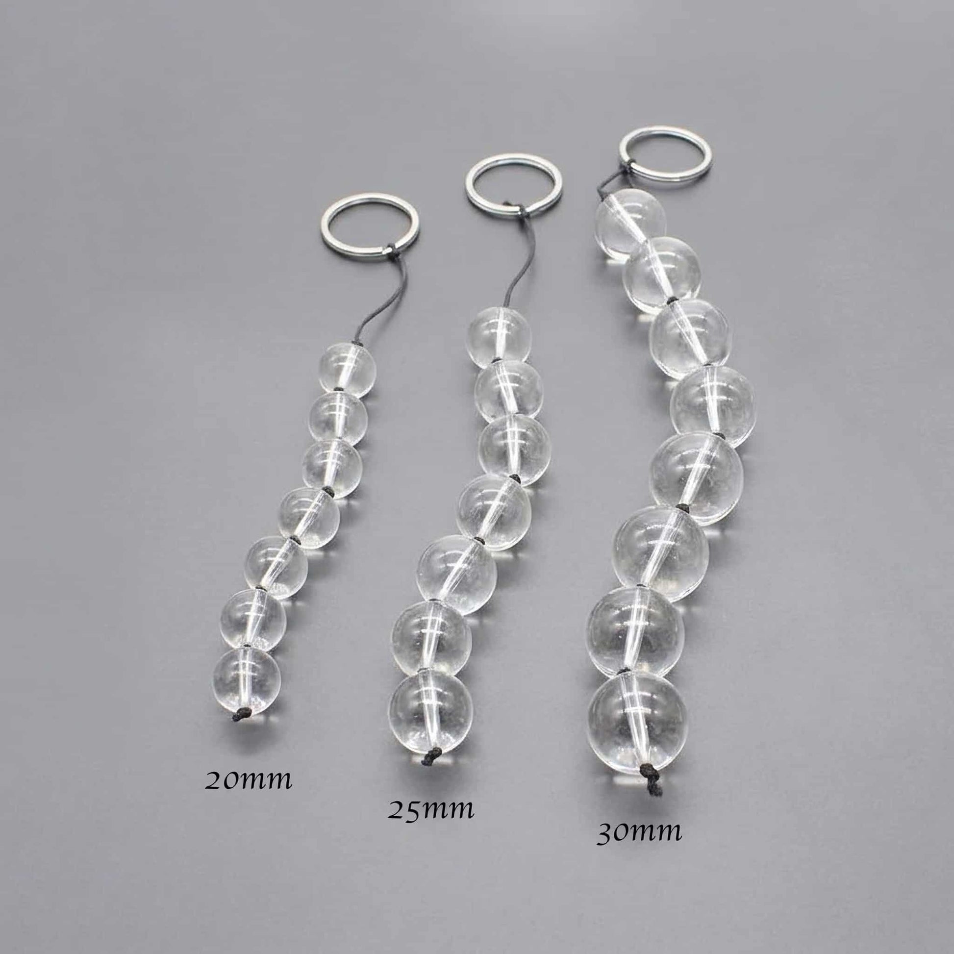 Demonstrate the gradation of pulled glass beads from the smallest to the largest size. Lining up four beads (e.g., 20mm, 25mm, 30mm) and shooting them at an angle highlights the difference in size. The background is a clean gray to make the beads stand out.