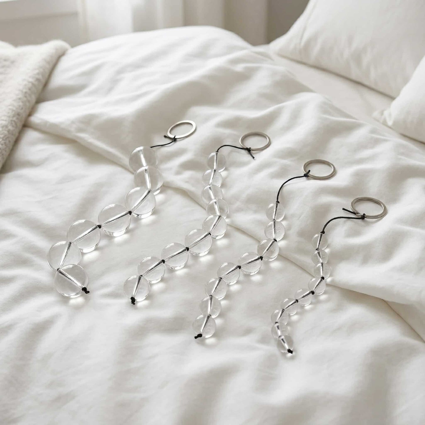 The glass pull bead is placed on a clean, soft white sheet. It curves naturally and contrasts with the sheet. The lighting is soft, creating a feeling of comfort and privacy. 