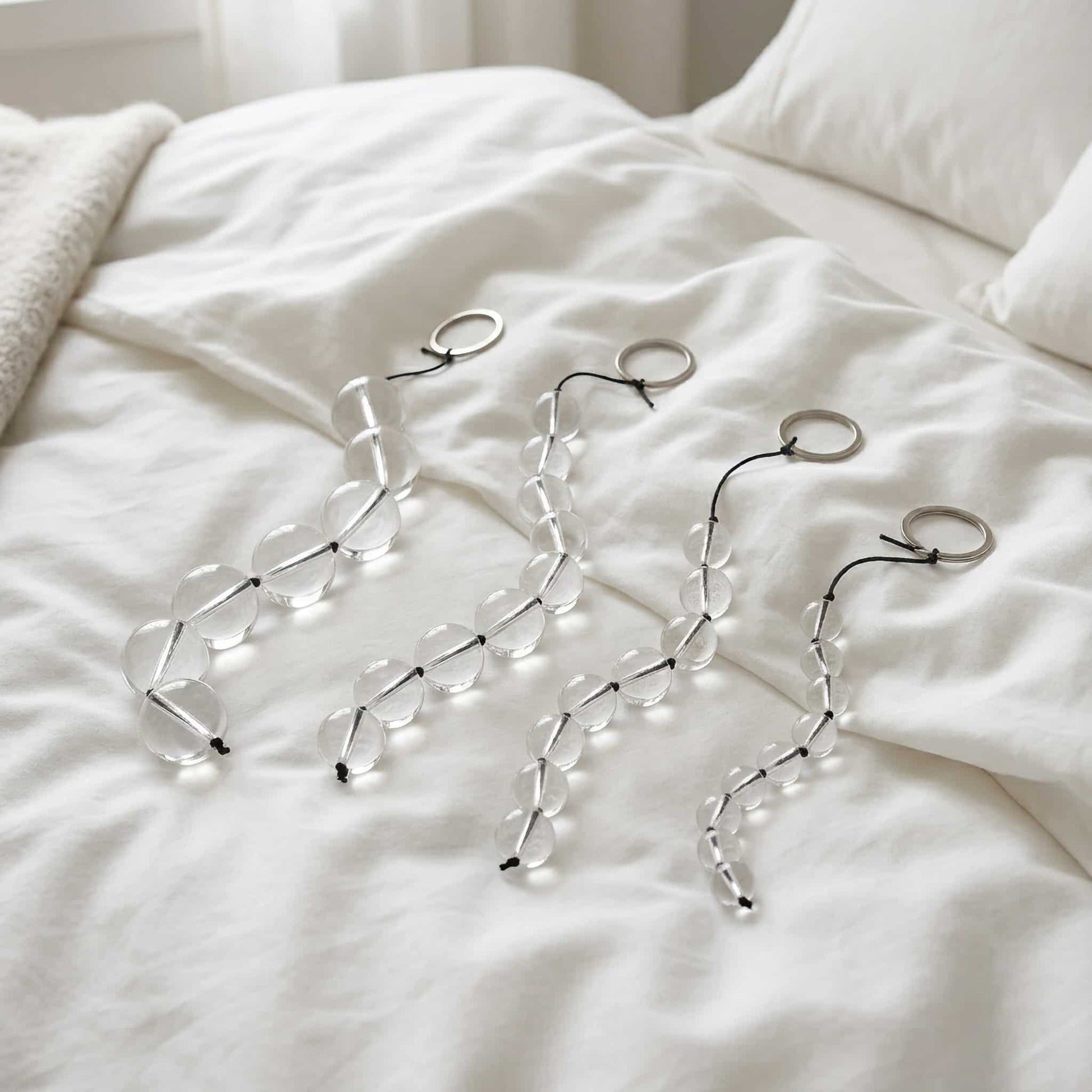 The glass pull bead is placed on a clean, soft white sheet. It curves naturally and contrasts with the sheet. The lighting is soft, creating a feeling of comfort and privacy. 