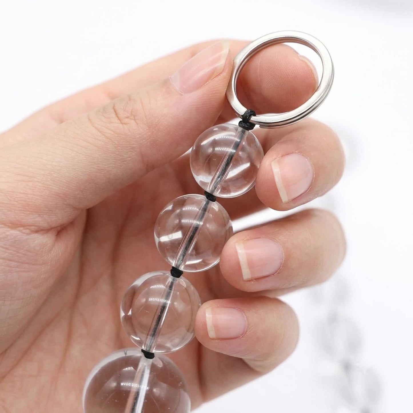 One hand gently holds the end of the glass pull bead, focusing on the first few glass beads and stainless steel rings. The hand has smooth skin and neatly trimmed nails. Close-ups highlight the shine and smoothness of the beads and the metallic texture of the rings.