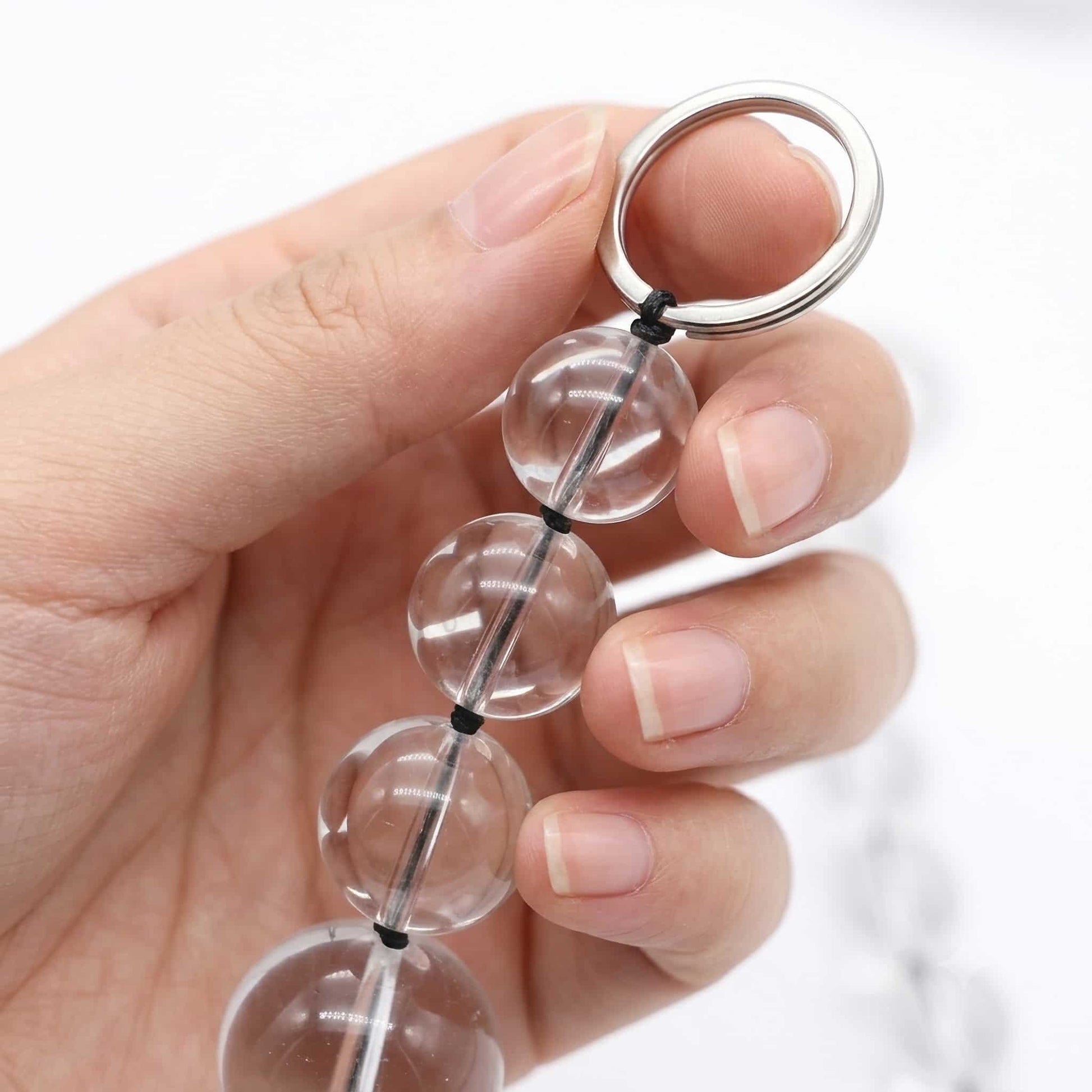 One hand gently holds the end of the glass pull bead, focusing on the first few glass beads and stainless steel rings. The hand has smooth skin and neatly trimmed nails. Close-ups highlight the shine and smoothness of the beads and the metallic texture of the rings.