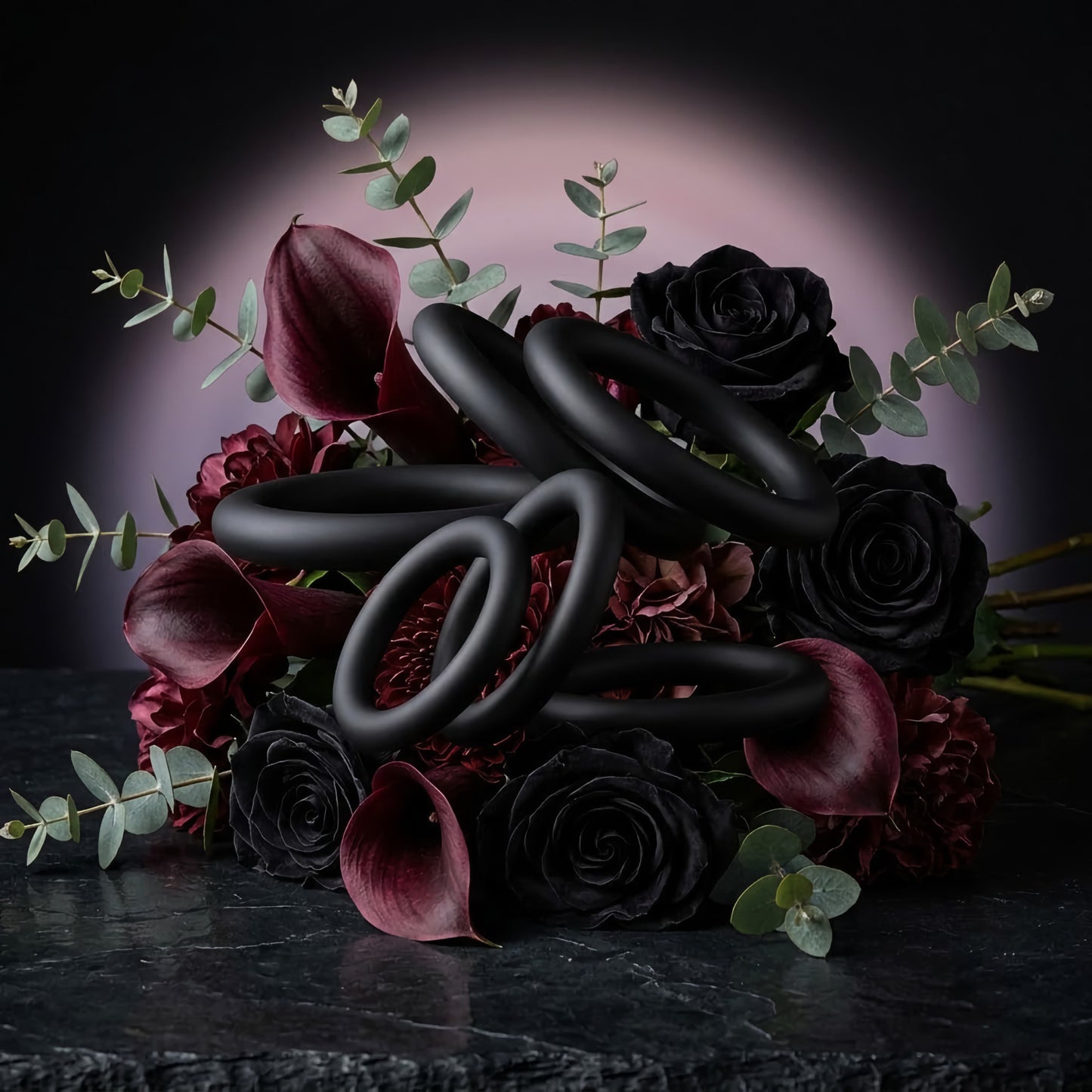Black silicone cock ring set with multiple sizes arranged in a luxurious bouquet of black roses and burgundy calla lilies. Premium sensual adult wellness accessories.