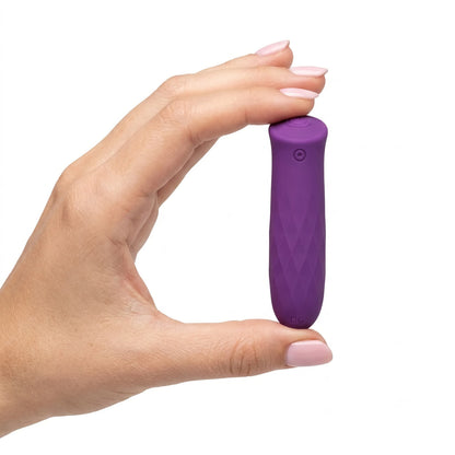 Clean product photo showing a manicured hand with pink nail polish gently holding the deep purple massager between the thumb and forefinger, providing a scale comparison to emphasize its small, discreet, and pocket-sized design.