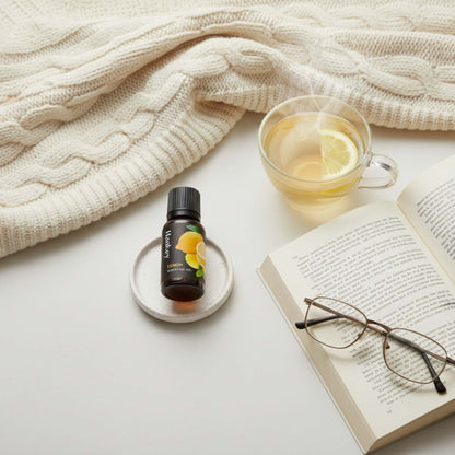 Lemon essential oil bottle next to an open book and a cup of tea, enhancing a cozy reading and relaxation moment.