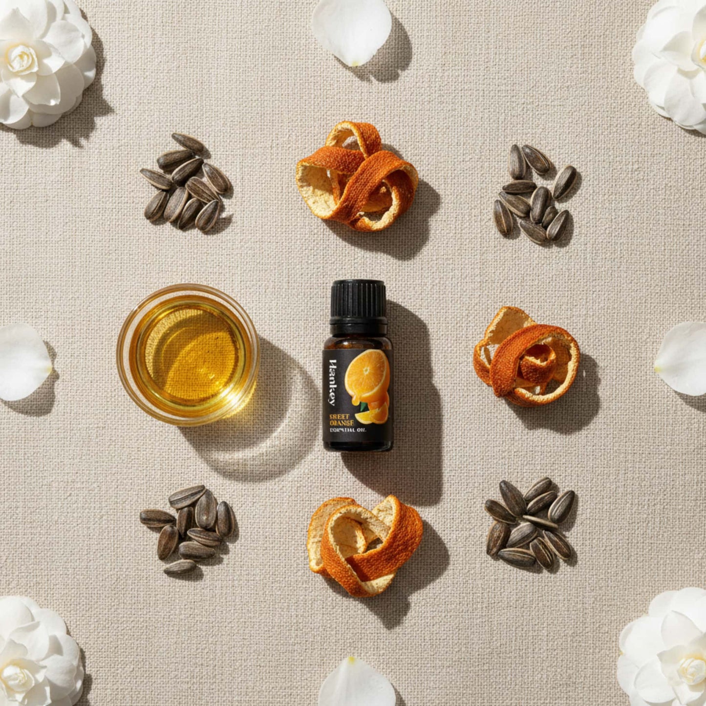Flat lay overview of Sweet Orange blend ingredients: bottle, orange peels, camellia petals, and sunflower seeds on linen.