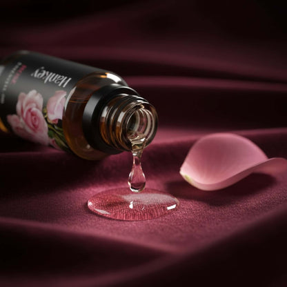 Macro shot of Rose essential oil dripping from the bottle neck onto luxurious deep burgundy velvet fabric, emphasizing its rich texture and dropper dispenser.